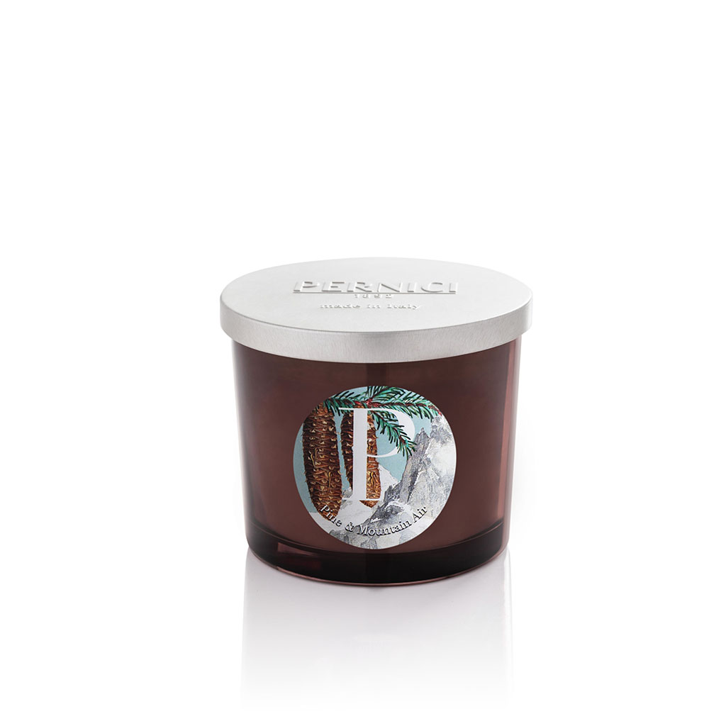 Candela profumata Pine & mountain air 200 g in vaso di vetro ambrato, fotografata accesa su sfondo neutro.